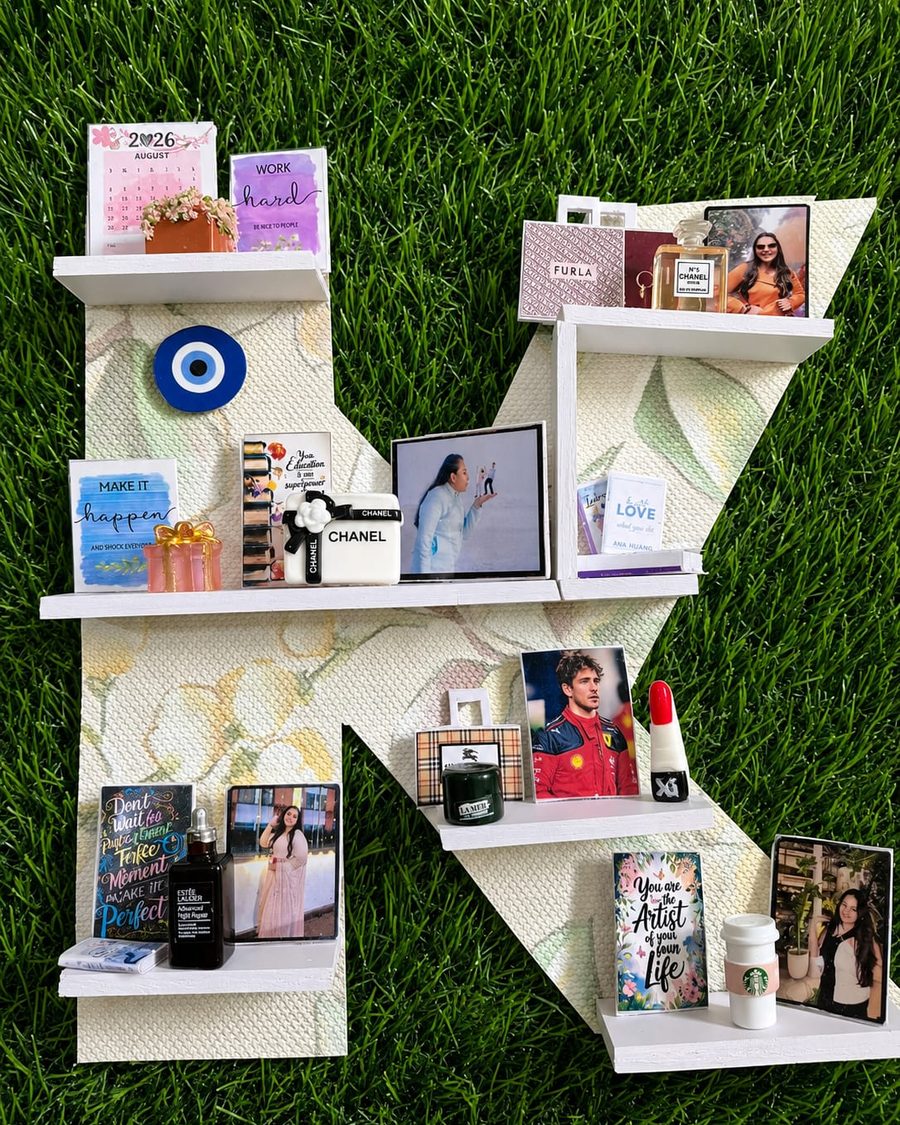 A letter-shaped Memory Wall in pale floral, holding photographs, perfume, books and small mementoes.