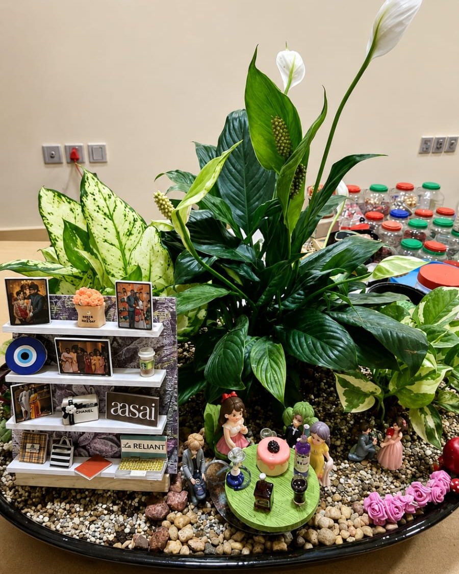 A large planted arrangement with a Peace Lily, gravel, small figures and a personalised display shelf set into it.