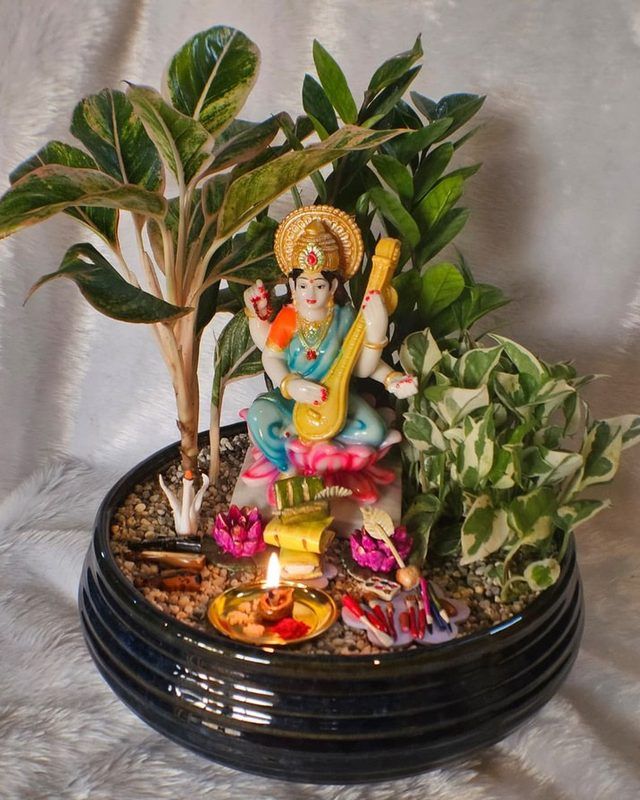 A planter built around a seated deity figure, with lit diyas and lotus flowers.