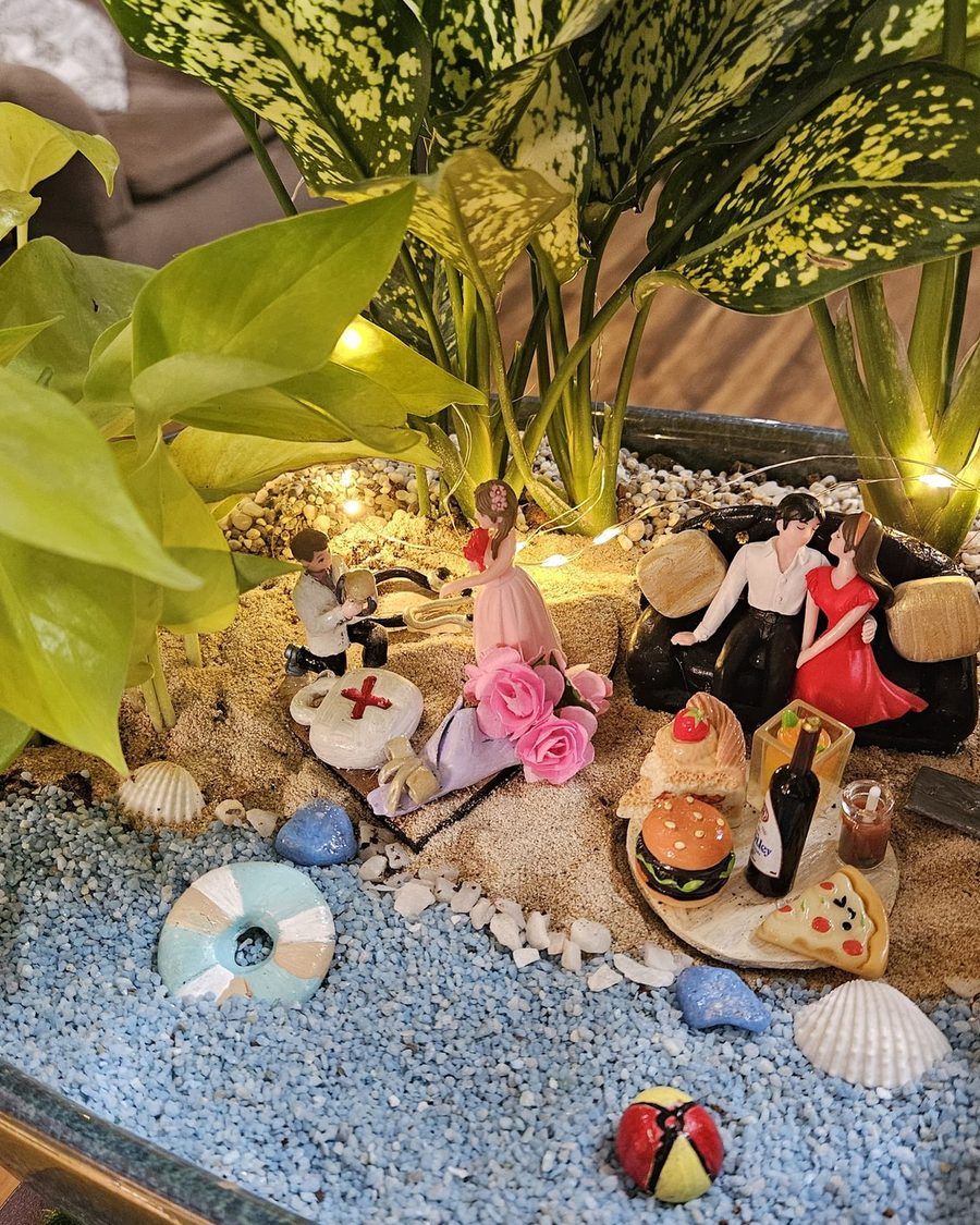 A shoreline built in miniature with pale sand, shells and two small figures among the planting.